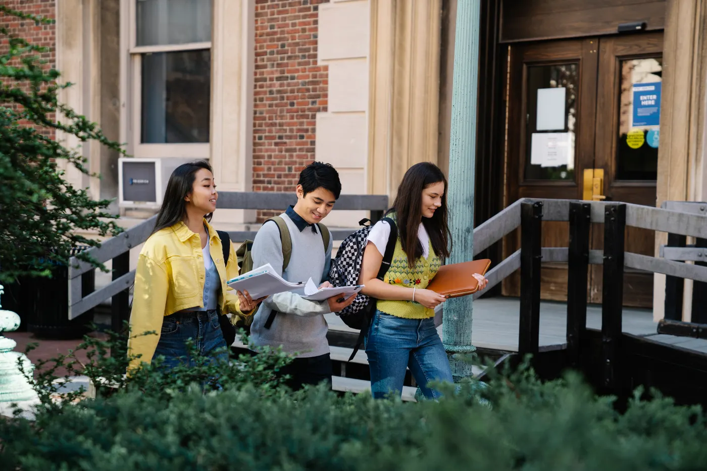 Three students walking across campus with books and notes